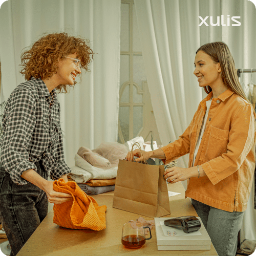 Lojista sorrindo enquanto entrega uma sacola de compras a uma cliente, ilustrando a oferta de cashback sem burocracia da Xulis.