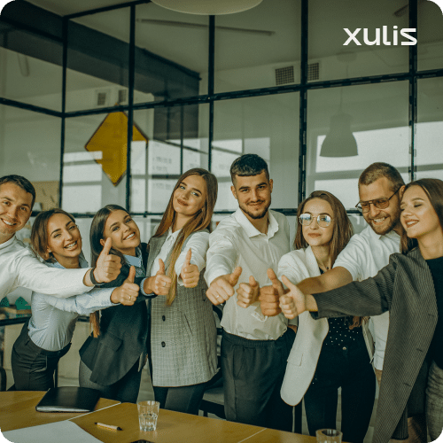 Equipe de clientes empresariais satisfeitos com a parceria da Xulis, todos fazendo um sinal de positivo em um escritório moderno.